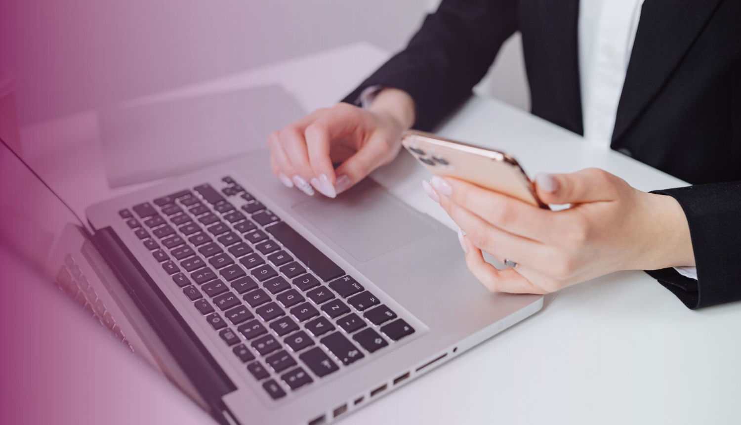 Sieviete strādā pie portatīvā datora, vienā rokā turot telefonu