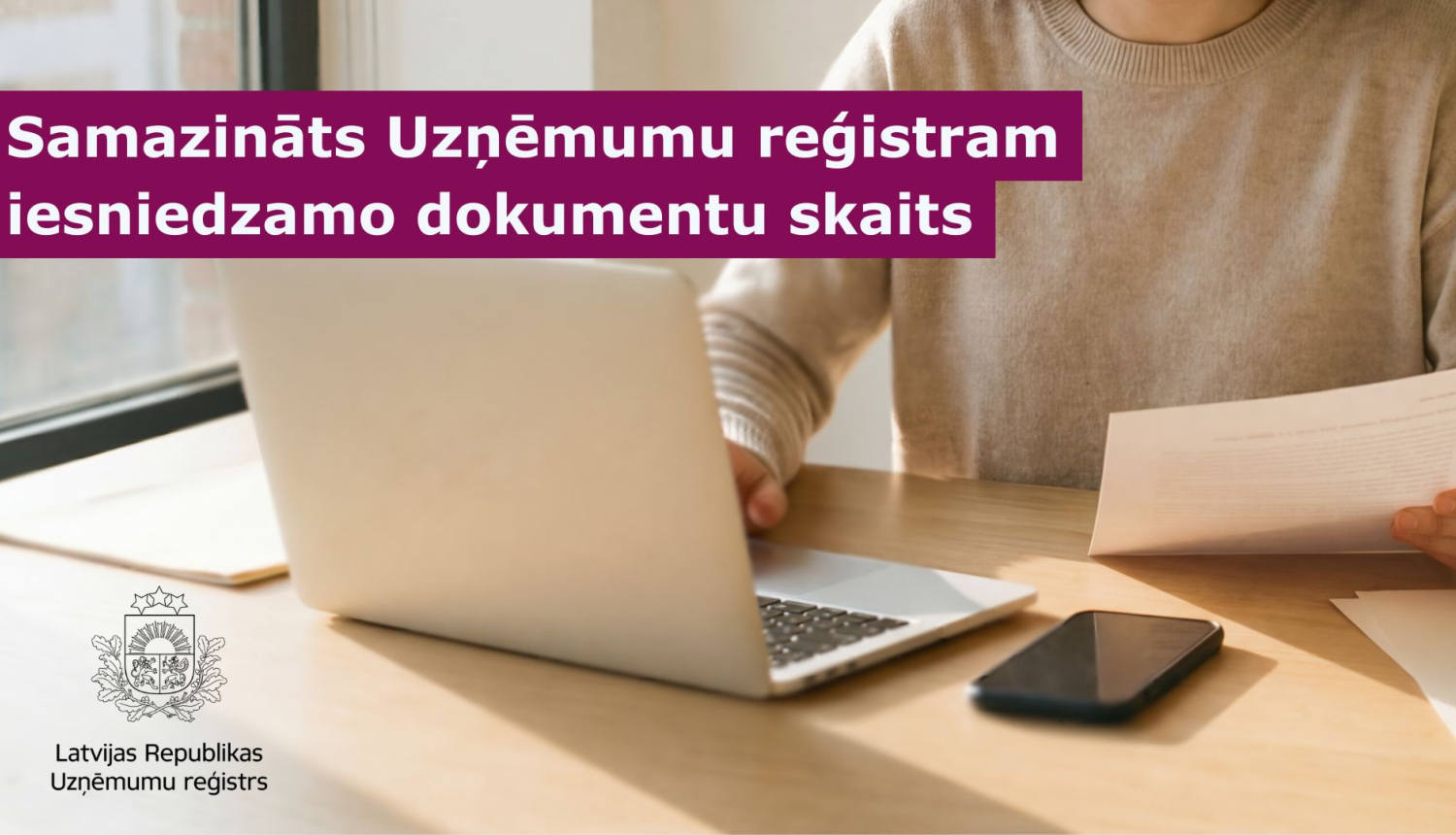 Persona sēž pie rakstāmgalda un strādā pie portatīvā datora