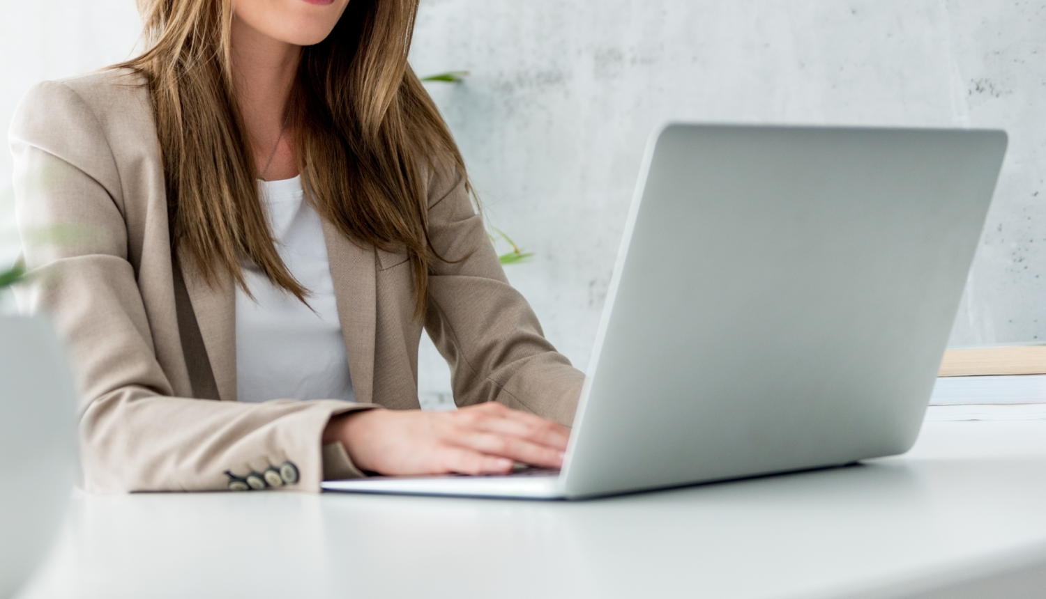 Sieviete sēž pie rakstāmgalda un raksta portatīvajā datorā